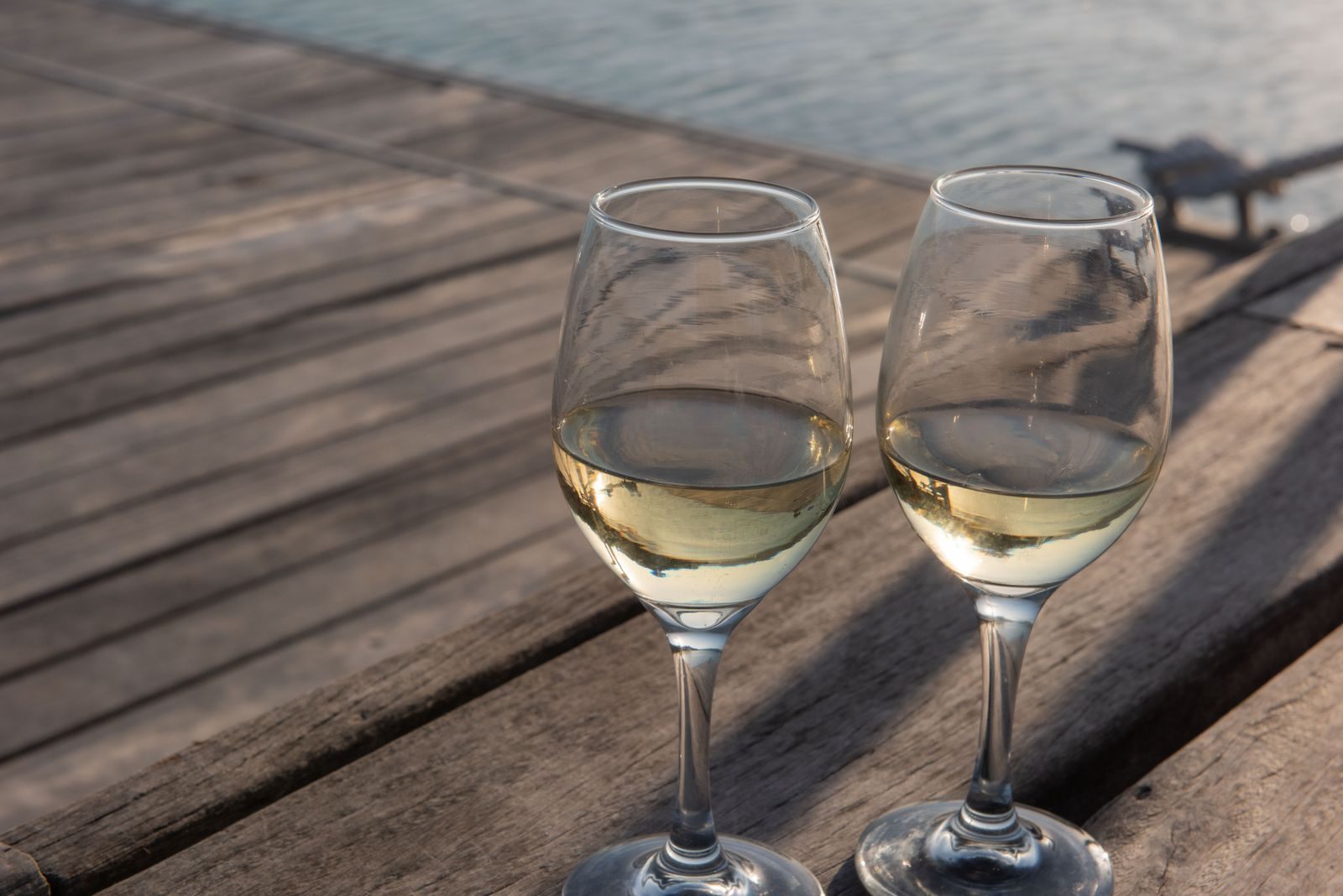 Two wine glasses on a wooden deck beside the water at sunset
